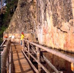 Sito graffiti: passerella sull'acqua, visitatore, roccione verticale sull'acqua, bosco
